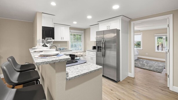 A modern kitchen with a stainless steel refrigerator, white cabinets, and a marble countertop. - 3BR Guest Escape w/ Pool & Theater (Palm Harbor)