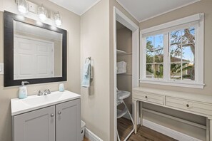 Un baño con tocador blanco, un espejo grande y una ventana con vistas a árboles.