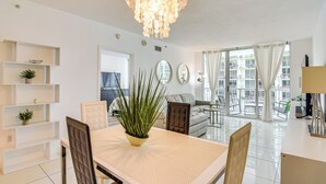 Un salon moderne comprenant une table à manger, des chaises, une plante en pot et une grande fenêtre donnant sur des immeubles.