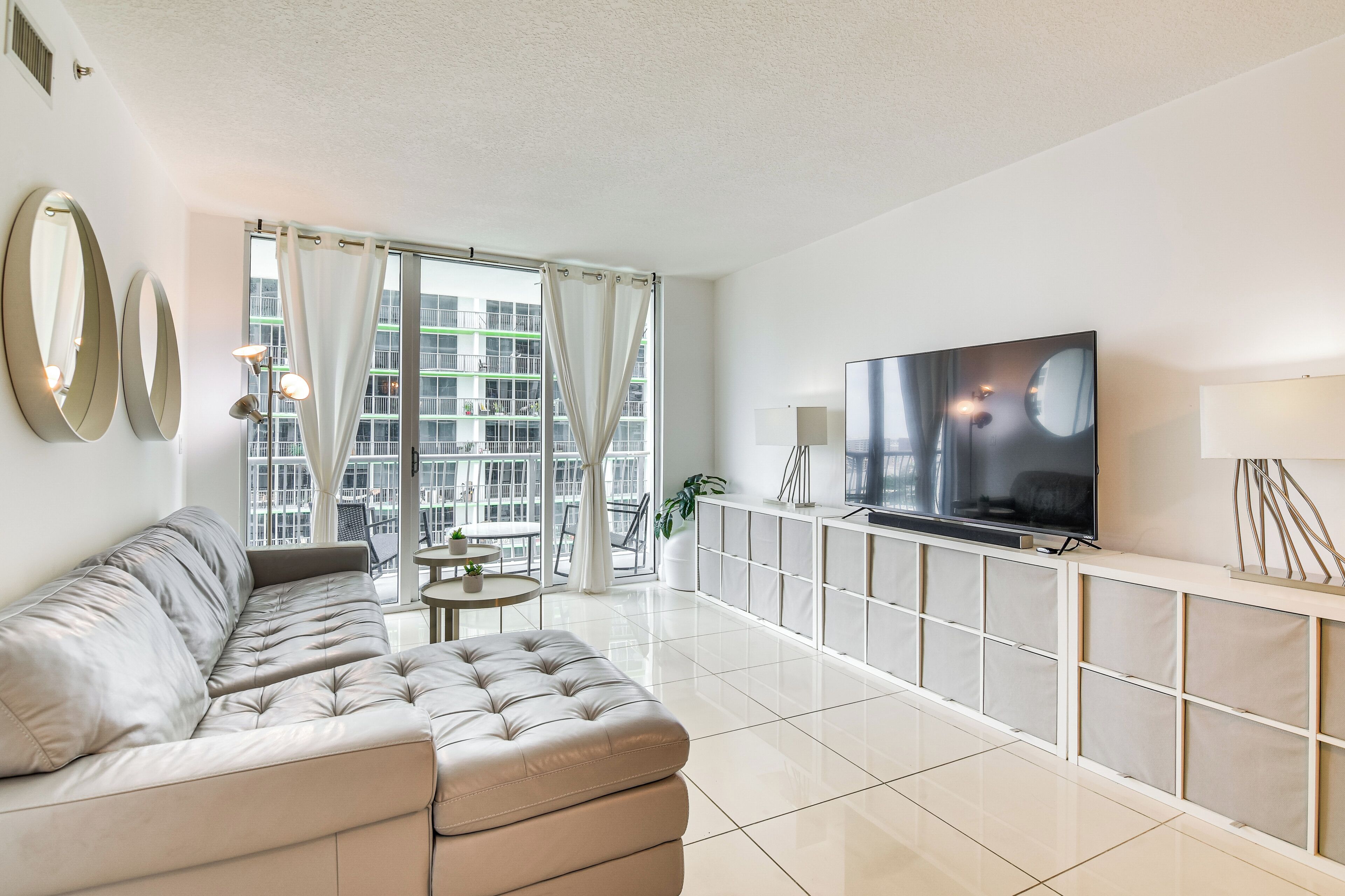 A modern living room with a sofa, a TV, a small table, and a balcony with curtains.