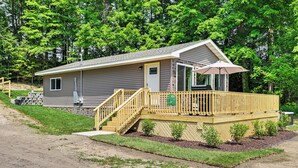 A single-story cabin with a wooden deck, a small porch, and a door leading to the main entrance. - Deck, Dock & Hot Tub: Lakeside Retreat in Michigan (Hartford)