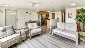 A modern living room with a sofa, chairs, a small table, and a kitchen in the background. - Deck, Dock & Hot Tub: Lakeside Retreat in Michigan (Hartford)