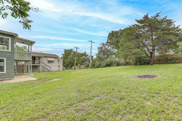 A residential backyard with a grassy lawn, a small tree, and a house with a porch.