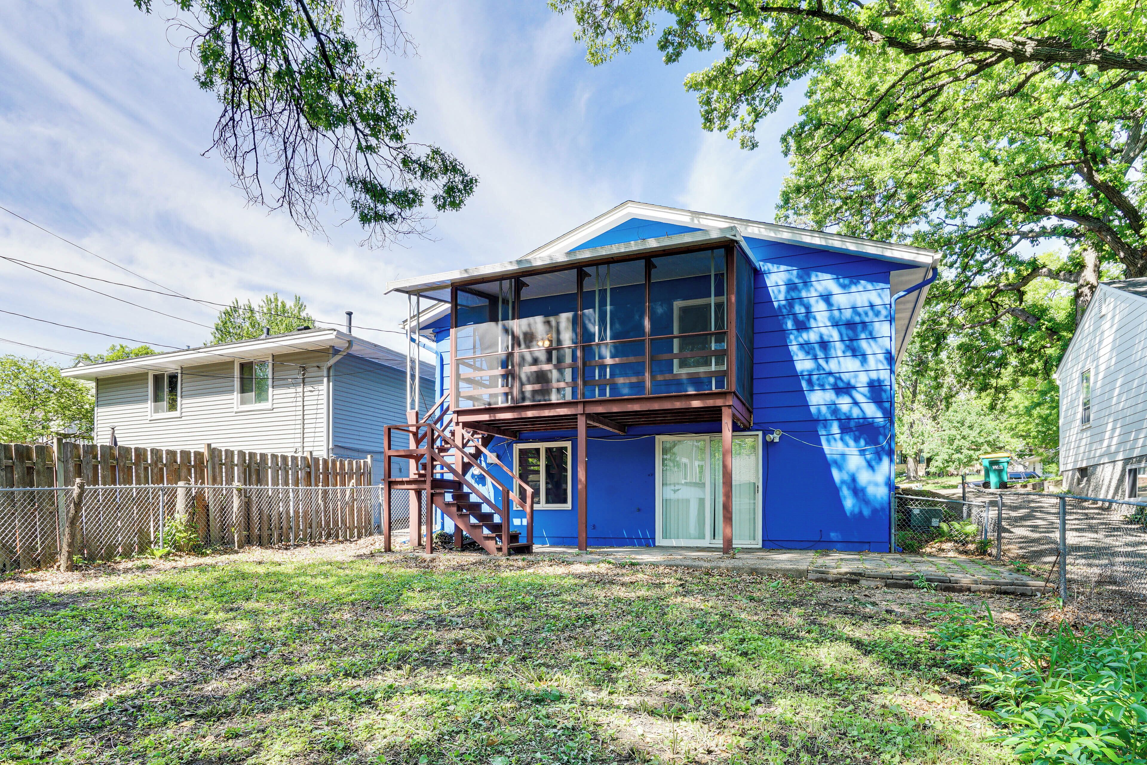 Une maison à deux étages, avec une façade bleue, une terrasse en bois et un escalier menant à l’étage supérieur.