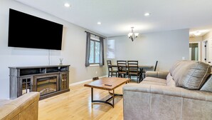 Ein Wohnzimmer mit Flachbildfernseher, Holzboden, einer Couch, einem Esstisch mit Stühlen und einem Kamin.