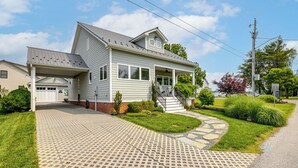 A two-story house with a covered garage, a front porch, and a landscaped driveway. - Near Solomons Island Boardwalk: Home w/ Hot Tub! (Solomons)
