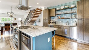 A modern kitchen with a central island, stainless steel appliances, and a wooden staircase. - Near Solomons Island Boardwalk: Home w/ Hot Tub! (Solomons)