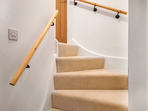 Un escalier recouvert de moquette, doté d’une main courante en bois et de rampes fixées au mur, de couleur noire.