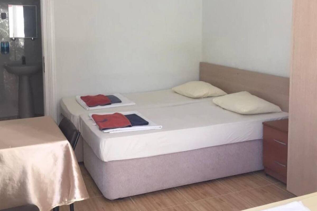Une petite pièce, bien rangée, avec un lit, une table et un lavabo.