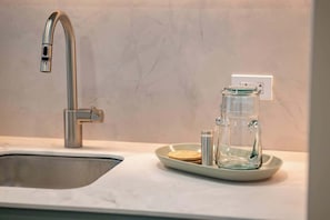 A kitchen with a modern stainless steel sink, a glass coffee maker, and a small plate with a wooden coaster.