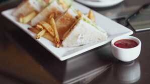 Une assiette de sandwichs et de frites sur une table, avec une tasse de café et un petit bol de sauce.