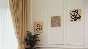 Un salon moderne avec un canapé d’angle, une table basse en verre aux pieds dorés et des œuvres d’art accrochées au mur.