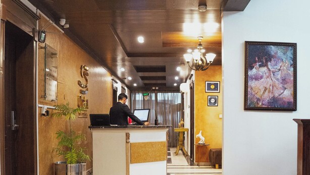 Un hall d’hôtel avec un comptoir d’accueil, une plante en pot, un tableau accroché au mur et un sol en marbre.
