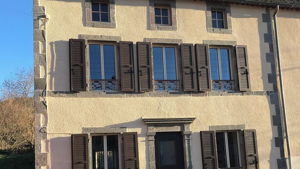 A two-story building with a symmetrical facade, featuring a central entrance with a black door and windows with shutters. - Charming house (Saint-Nectaire)