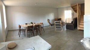A spacious living area with a dining table, chairs, a sofa, and a staircase. - Charming house (Saint-Nectaire)