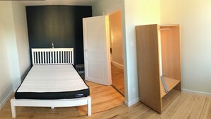 A bedroom with a white bed, a dark wall, and a wooden floor. - Charming house (Saint-Nectaire)