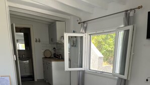 Et soveværelse med en seng, et vindue med gardiner, udsigt til et køkken og en dør til et andet rum.