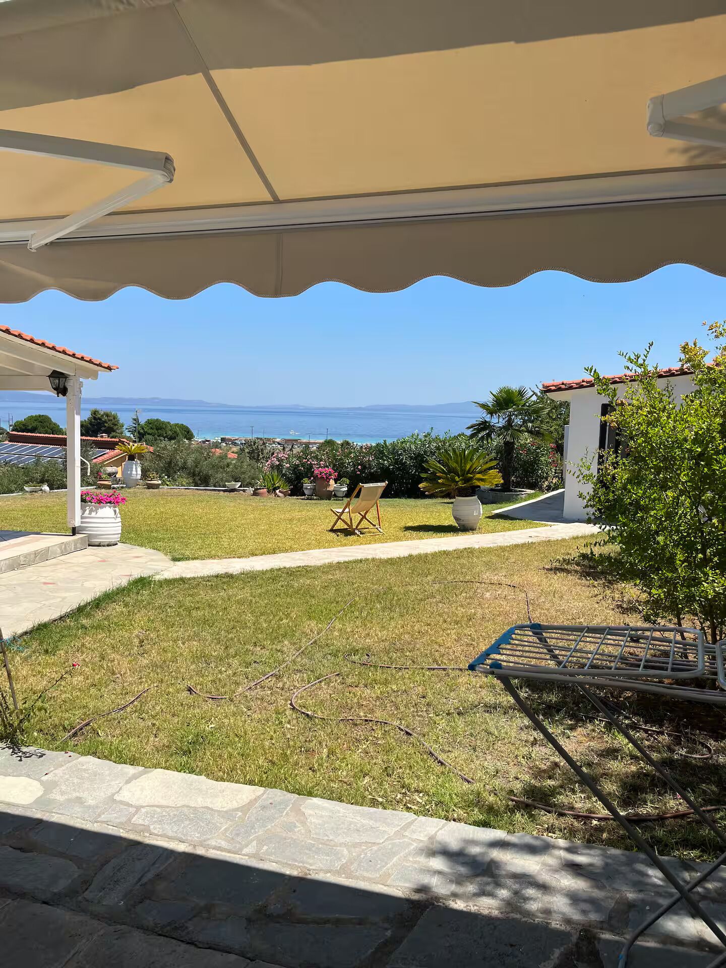 A covered outdoor area with a view of the sea, a lawn, and a chair.