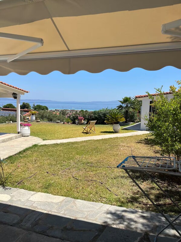 A covered outdoor area with a view of the sea, a lawn, and a chair.