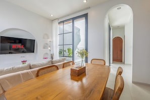 Un espace repas moderne avec une table en bois, des sièges rembourrés, un vase avec des fleurs et un téléviseur diffusant du contenu « NETFLIX ».