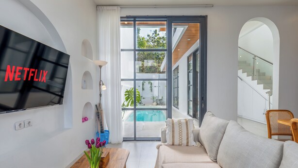 Un salon moderne doté d’un téléviseur à écran plat, d’un canapé, d’une table basse et offrant une vue sur une piscine.
