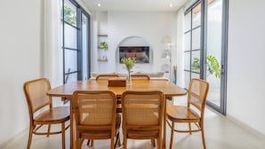 Un coin repas avec une table en bois et six chaises en osier, un vase rempli de fleurs et un téléviseur fixé au mur affichant le logo de Netflix.