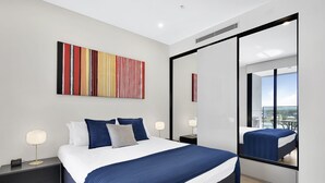 Une chambre d’hôtel moderne avec un grand lit, une porte-fenêtre coulissante donnant sur un balcon, une peinture abstraite aux couleurs vives et une vue sur la ville.