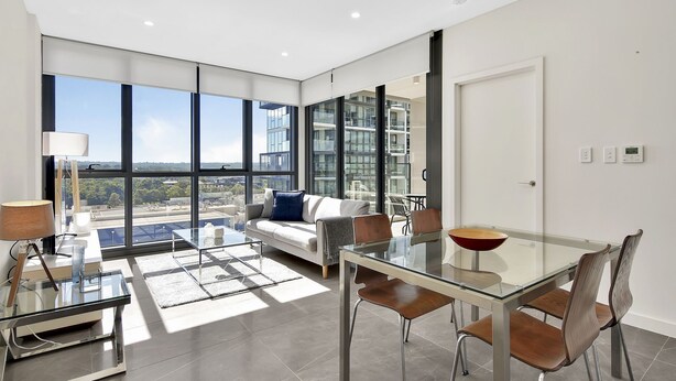 Un salon moderne avec une table à manger en verre, un canapé et une vue sur le paysage urbain grâce à de grandes fenêtres.