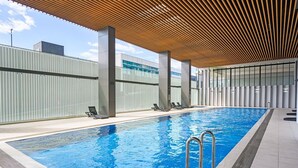 Une piscine intérieure moderne, avec une eau d’un bleu cristallin, entour ée de chaises longues et dotée d’une structure de plafond en bois.