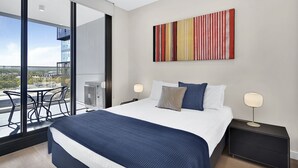 Une chambre d’hôtel moderne, dotée d’un grand lit, de deux tables de chevet, d’un ventilateur de plafond et d’une grande fenêtre donnant sur un panorama urbain.