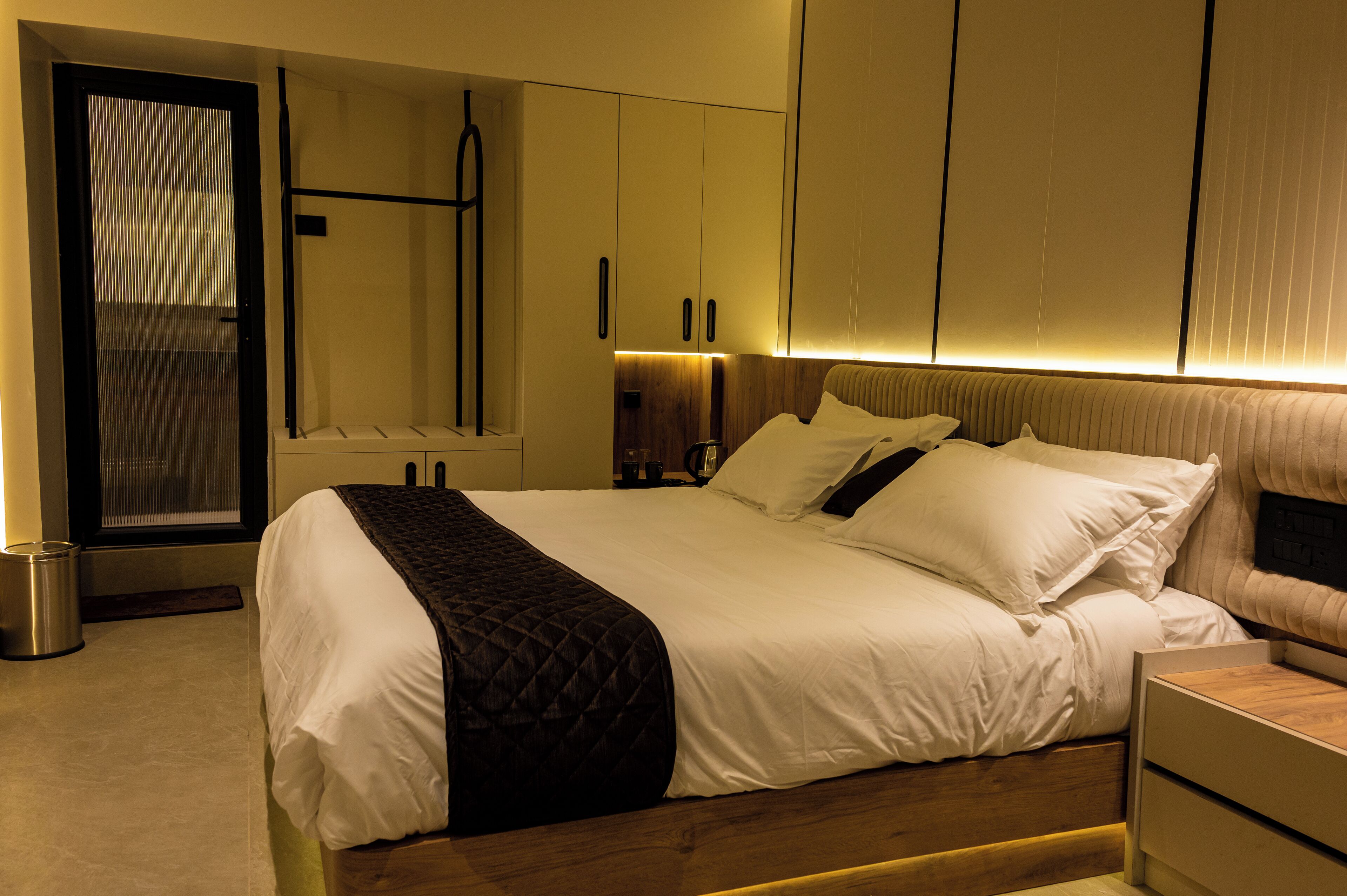 Ein modernes Hotelzimmer mit einem großen Bett, einem Nachttisch, einem Kleiderschrank und einem Spiegel.