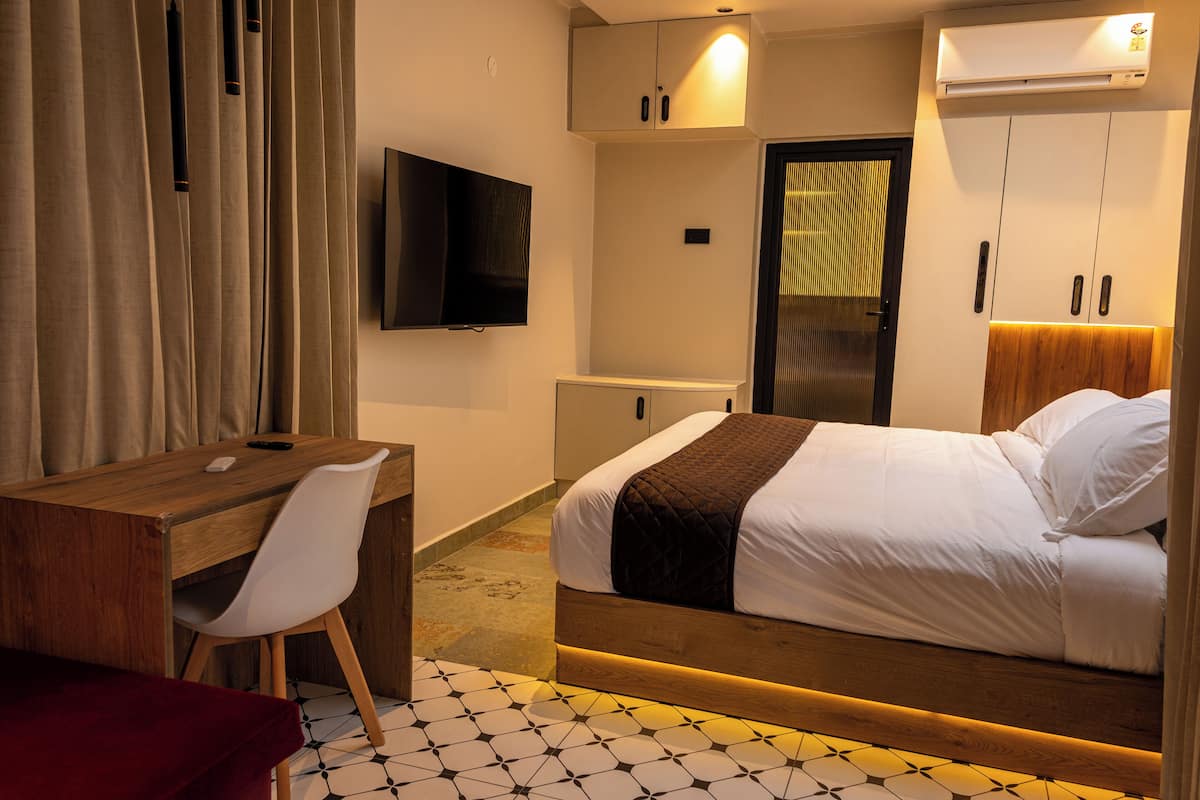 A hotel room with a bed, a desk, a chair, a TV, and a wardrobe.