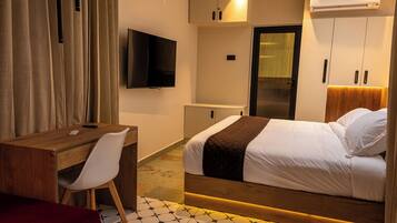 A hotel room with a bed, a desk, a chair, a TV, and a wardrobe.