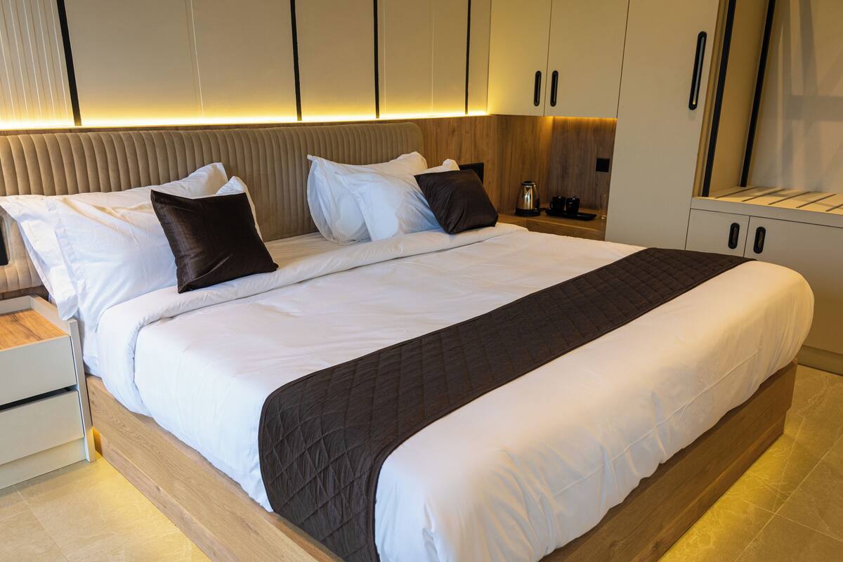 A modern hotel room with a large bed, a bedside table, and built-in cabinets.