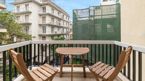 A balcony with two wooden chairs and a small table, overlooking a cityscape with multi-story buildings and a construction site. - Central Downtown Living (Athina)