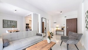 A modern living room with a sofa, armchair, and coffee table. There is a kitchen area visible in the background.
