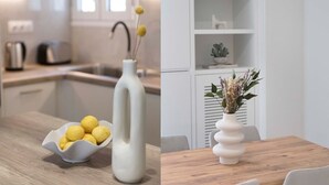 A modern kitchen with a white countertop, a bowl of lemons, and a white vase with yellow flowers.