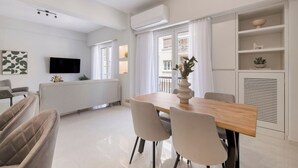 A modern living room with a dining area, a flat-screen TV mounted on the wall, and a built-in air conditioning unit.