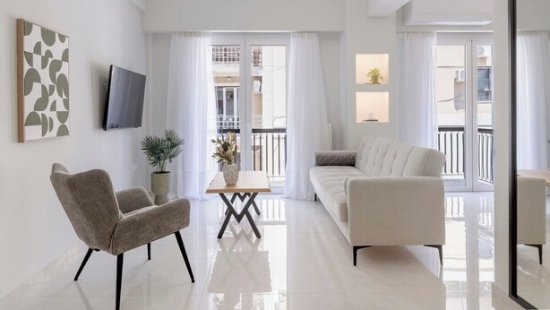 A modern living room with a sofa, two armchairs, a coffee table, and a TV mounted on the wall.