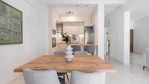 A modern dining area with a wooden table and grey chairs, a vase with flowers, and a kitchen in the background.