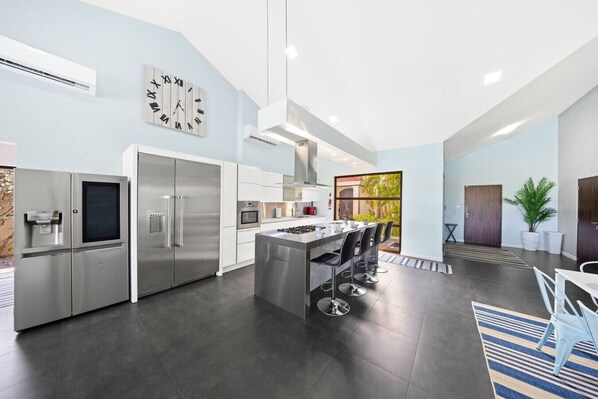 A modern kitchen with stainless steel appliances, a central island with bar stools, and a large window providing natural light.