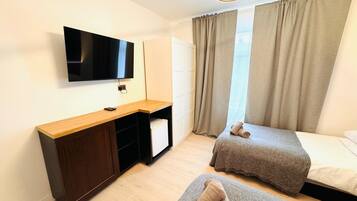Habitación de hotel con escritorio de madera, televisor de pantalla plana, dos camas y un ventanal con cortinas.