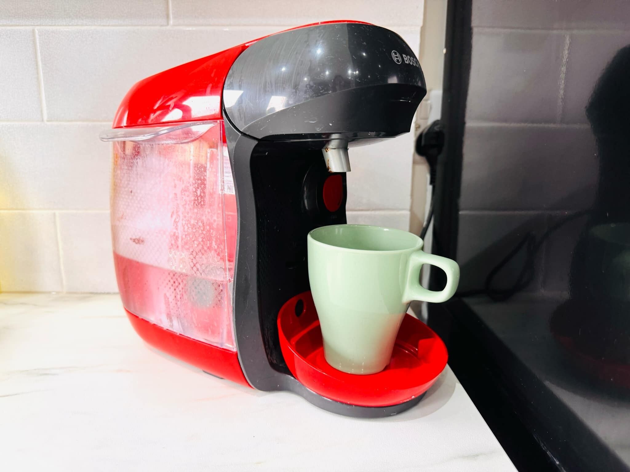 A red and black coffee maker with a green mug on its drip tray.