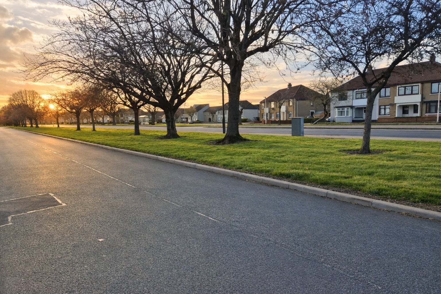 Rua residencial com casas, árvores e céu claro.