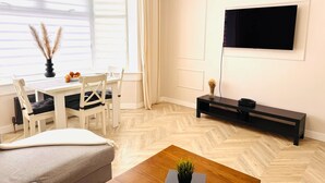 A modern living room with a sofa, a dining table with chairs, a TV mounted on the wall, and a wooden coffee table.