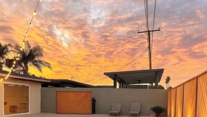 A modern outdoor pool area with a fire feature, lounge chairs, and a sunset view.
