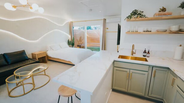 A modern bedroom with a large bed, a small bedside table, a glass coffee table, and a view of the outdoors.