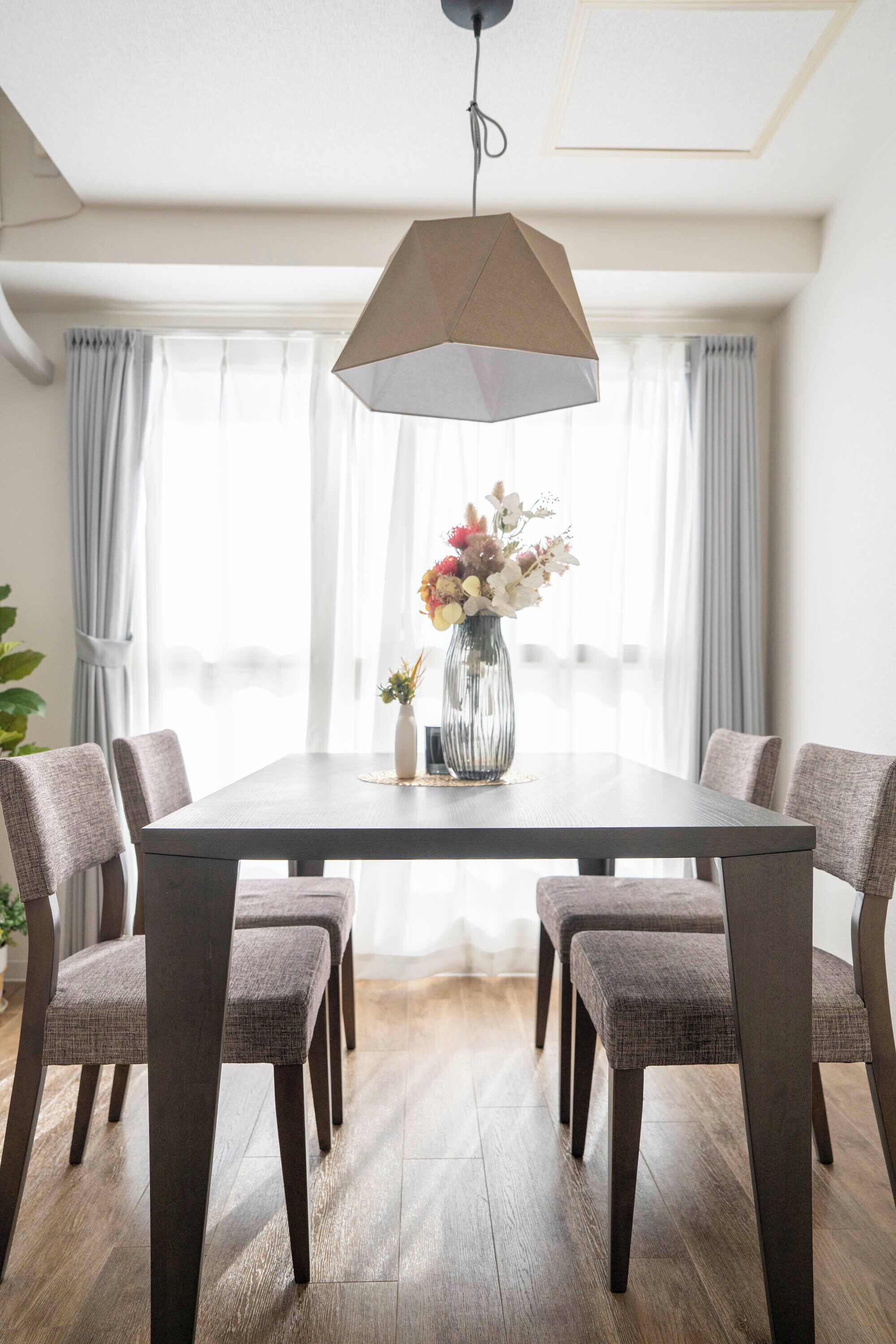 Un espace repas comprenant une table rectangulaire, six chaises rembourrées, un vase avec des fleurs et un luminaire suspendu.