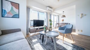 A modern living room with a sofa, a TV, a dining area, and a large window. - E-US NAEBO601 (Sapporo)