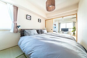A bedroom with a large bed, a bedside table, a lamp, a mirror, and a window with curtains. - E-US NAEBO601 (Sapporo)